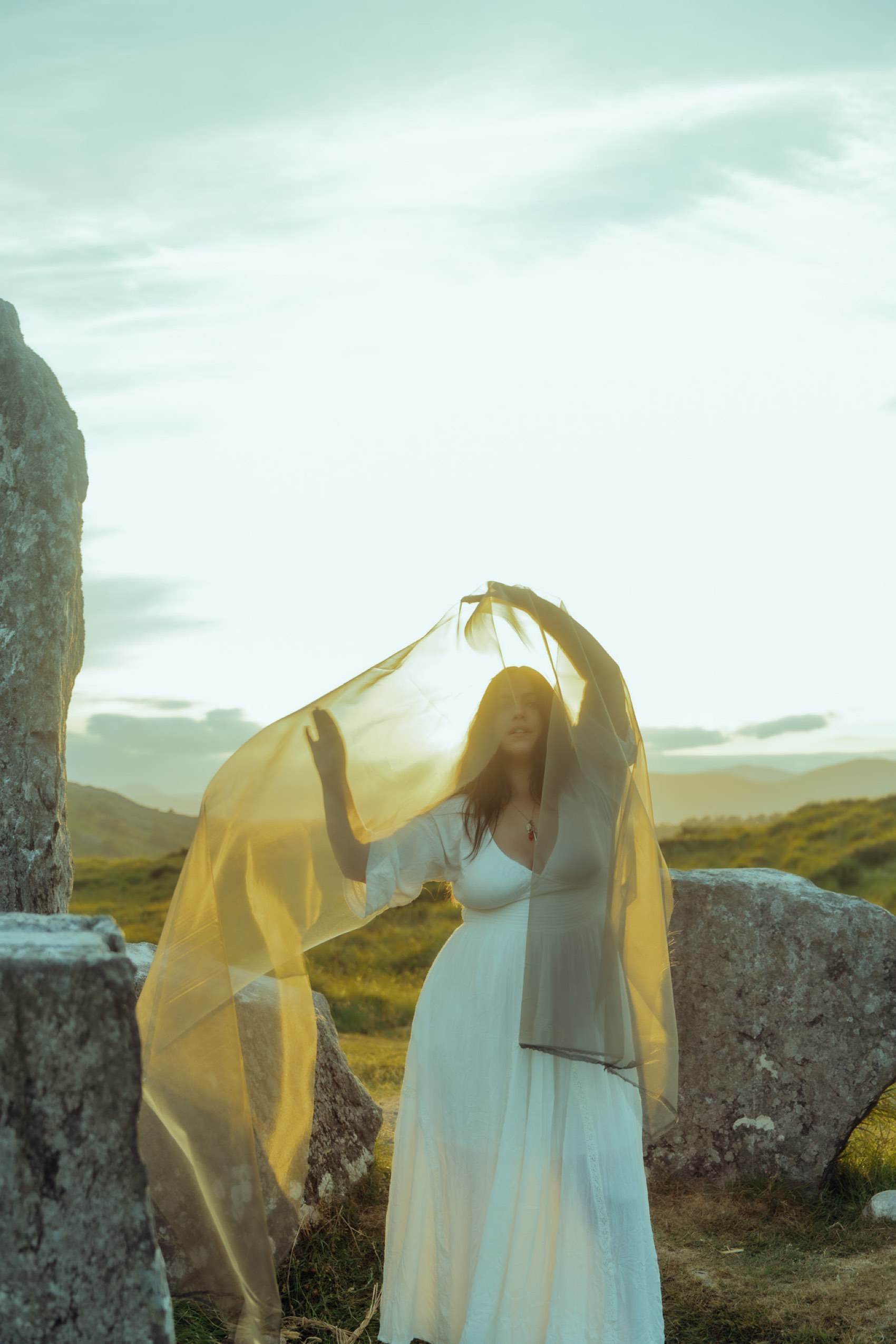 Natalie raising a golden veil among the standing stones at sunset