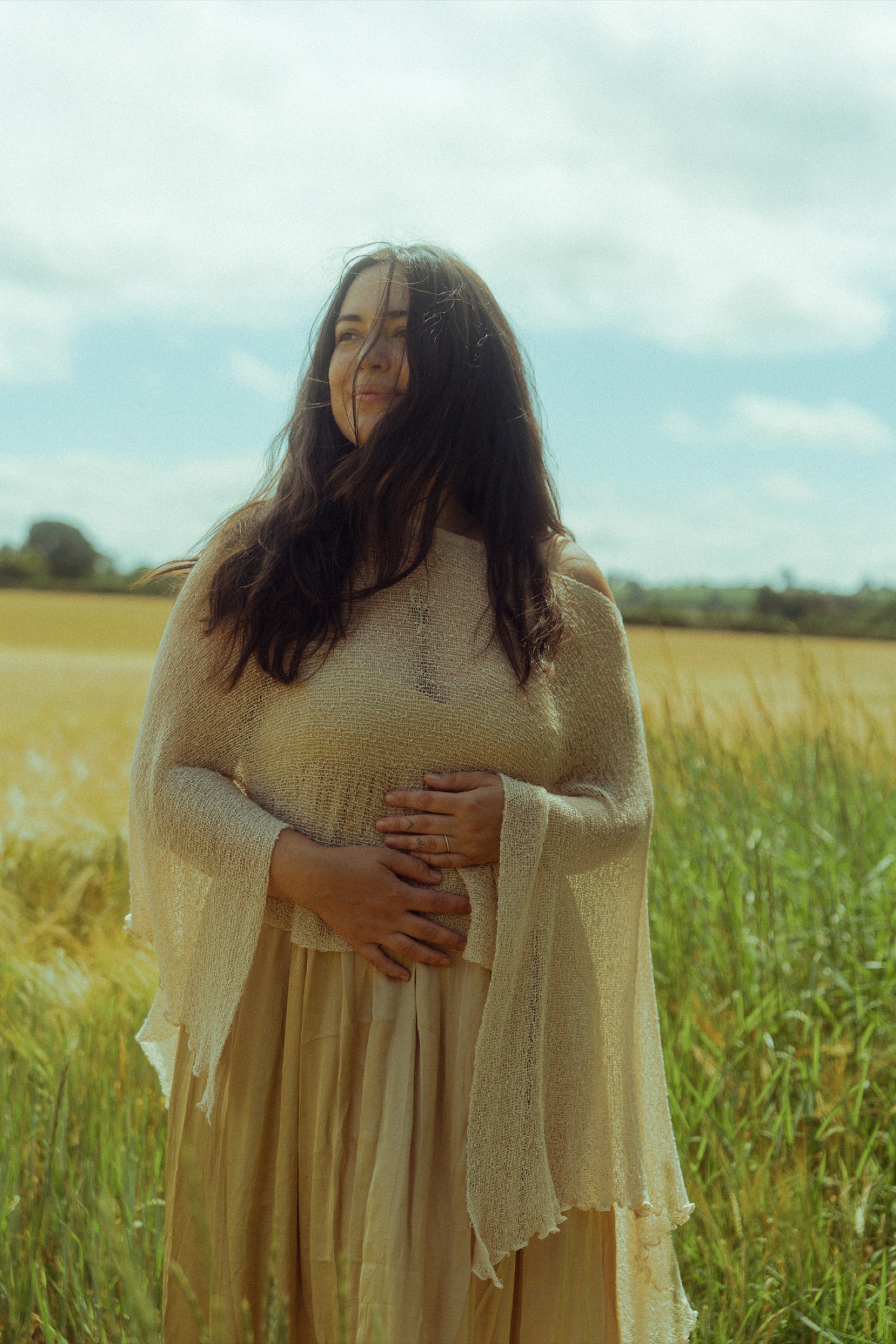 Natalie standing in a golden field, hands resting over her womb